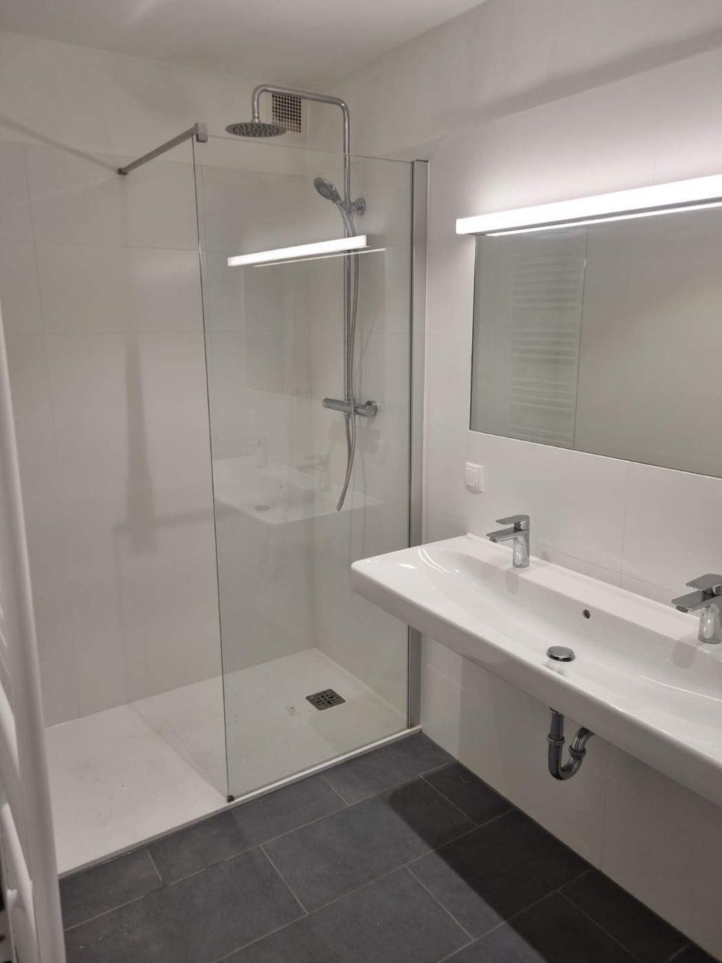 Fertiggestelltes helles Bad mit Regendusche, Glasabtrennung und Doppelwaschbecken